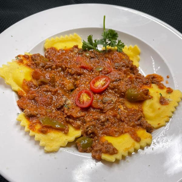 Figaretti's ravioli topped with rich meat sauce, cherry tomatoes, and fresh parsley on a white plate.