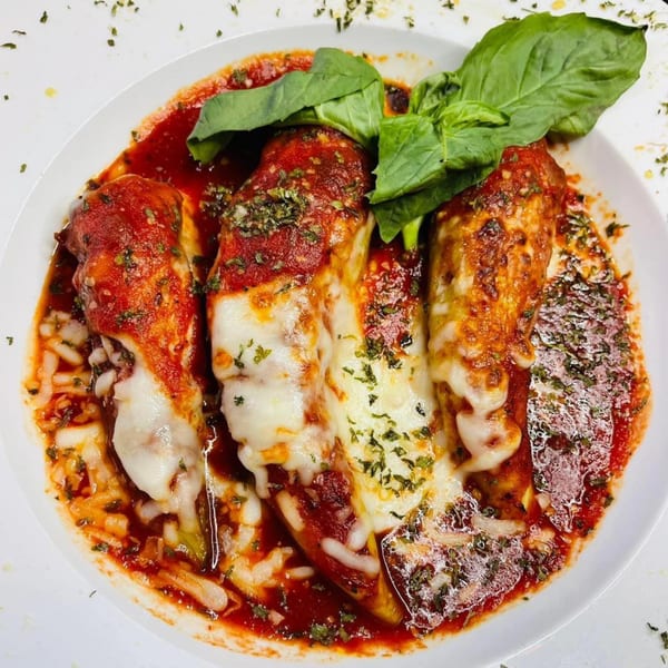 Three cheesy manicotti pasta rolls covered in red sauce and fresh basil on a white plate.
