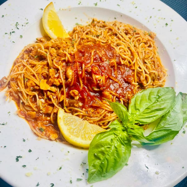 Figaretti's spaghetti with red sauce, lemon wedges, and fresh basil on a white plate.