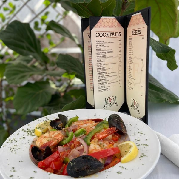 A vibrant seafood dish with mussels, shrimp, and colorful vegetables, alongside a Figaretti's cocktail menu.