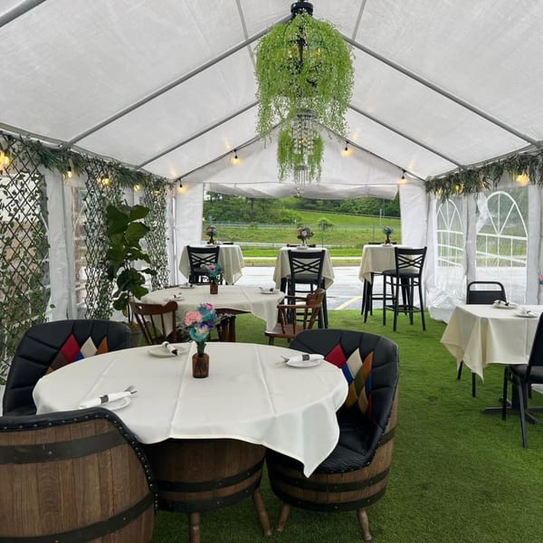 Outdoor dining tent with white tables, barrel chairs, and green turf flooring at Figaretti's Restaurant.