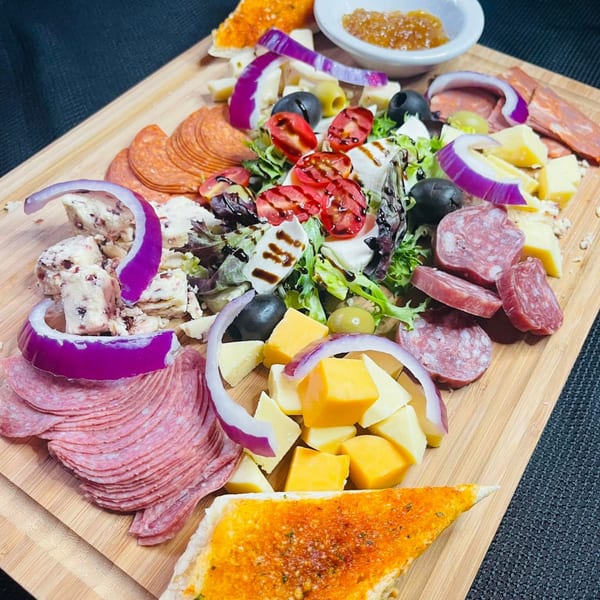 A wooden board filled with Italian meats, cheeses, olives, red onion, and a caprese salad.