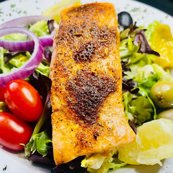 Grilled salmon fillet with a fresh salad of mixed greens, cherry tomatoes, red onions, and olives.